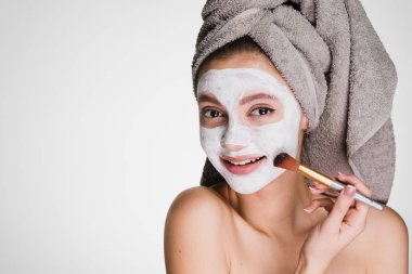 güzel genç kız başında bir havlu ile koyar yararlı beyaz bir maske yüzünde, gülümseyen