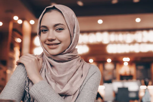 Vonzó muszlim lány fejkendő étteremben ül, várja őt étel, és mosolyogva — Stock Fotó