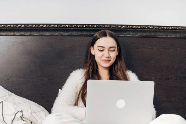 Hermosa chica sonriente en pijama se encuentra en la cama por la noche, viendo una película divertida en el ordenador portátil —  Fotos de Stock