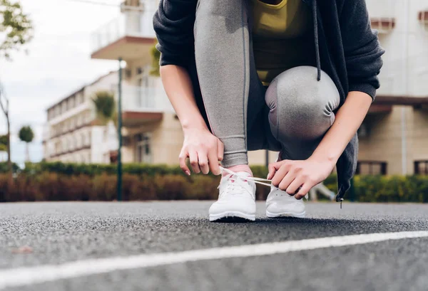 En ung flicka binder upp sin skosnören på sina sneakers, tåg på en utomhus idrottsplats — Stockfoto