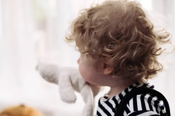 Malé kudrnatý blonďák, hrát si s jeho oblíbená Plyšová hračka — Stock fotografie
