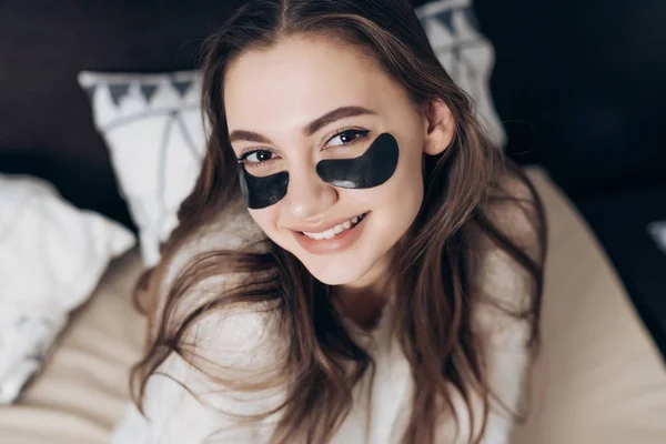 Χαρούμενη κοπέλα με πιτζάμες ξύπνησε νωρίς το πρωί, κάτω από τα μάτια του μαύρα μπαλώματα, χαμογελώντας — Φωτογραφία Αρχείου
