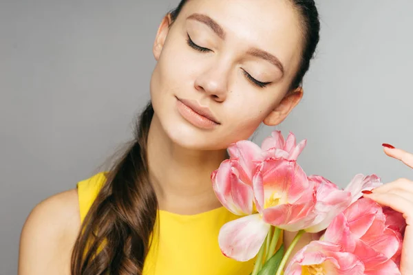 A magical young girl in a yellow dress enjoys the scent of pink flowers and in the spring, closed her eyes — Stock Photo, Image