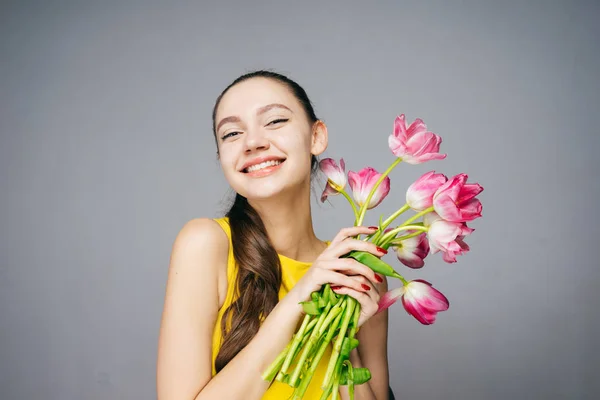 Een lachende jong meisje in een gele jurk houdt een boeket geurende roze bloemen, een goed humeur — Stockfoto