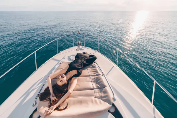 Привлекательная красивая девушка в черном платье лежит и расслабляется на корабле на солнце, долгожданный отпуск — стоковое фото