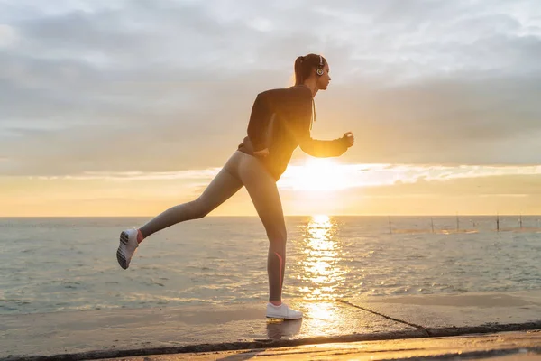 Envisa smal flicka springer runt havet i solnedgången, lyssna på musik i hörlurar — Stockfoto