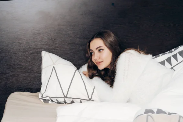 Schöne schöne Mädchen im weißen Pyjama liegt abends im Bett und ruht, lächelnd — Stockfoto