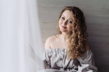 pencerenin yanında dinleniyor, kameraya bakıyor ve poz güzel elbise sevimli kıvırcık saçlı kadın