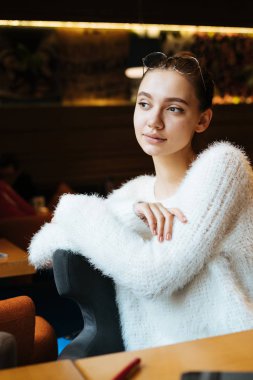 güzel düşünceli kız öğrenci okuldan sonra bir kafede oturup, pencereden dışarı bakarak ve bir şey hakkında düşünme beyaz ceket