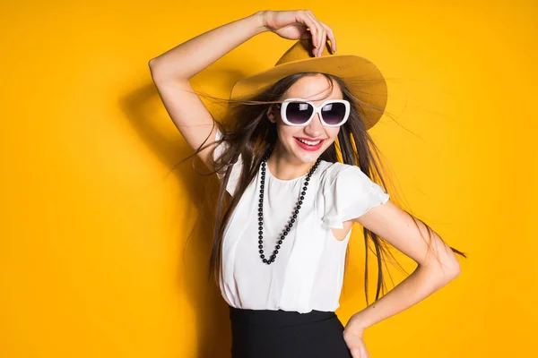 Ελκυστική κοπέλα μακρυμάλλης μοντέλο μόδας καπέλο και γυαλιά ηλίου, θέτοντας σε πορτοκαλί φόντο — Φωτογραφία Αρχείου