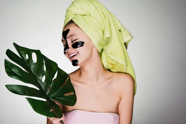 Красива дівчина сміється з зеленим рушником на голові наносила чорну маску для очищення на обличчя, денний спа-центр — стокове фото