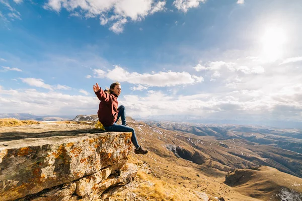 Счастливая молодая девушка путешествует по Кавказским горам, сидит на краю скалы — стоковое фото