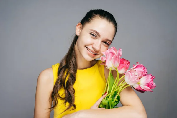 Alegre joven en vestido amarillo celebra, sostiene ramo de flores y sonrisas — Foto de Stock