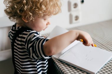 Beyaz not defterinde kıvırcık genç bebek şirin giysiler çizer