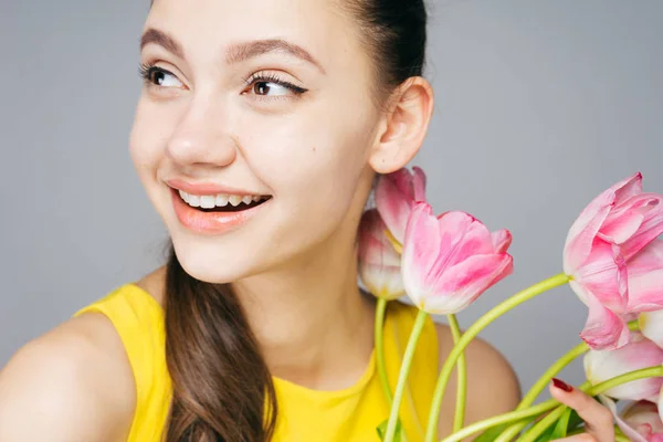Joyful charming girl with white teeth smiling, enjoying the spring, holding a bouquet of fragrant flowers — Stock Photo, Image