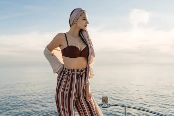 Mujer joven atractiva confiada en pantalones elegantes posando contra el mar en el sol —  Fotos de Stock