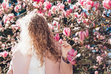 kıvırcık şık kadın çiçek açan bir Manolya güneşin yanında poz pembe bir ceket