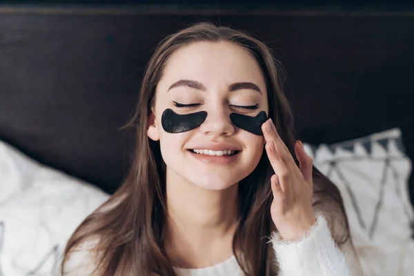 Όμορφη μακρυμάλλης κορίτσι ξύπνησε το πρωί σε μια καλή διάθεση, κάτω από τα μάτια του μαύρα μπαλώματα εναντίον πρήξιμο, χαμογελώντας — Φωτογραφία Αρχείου