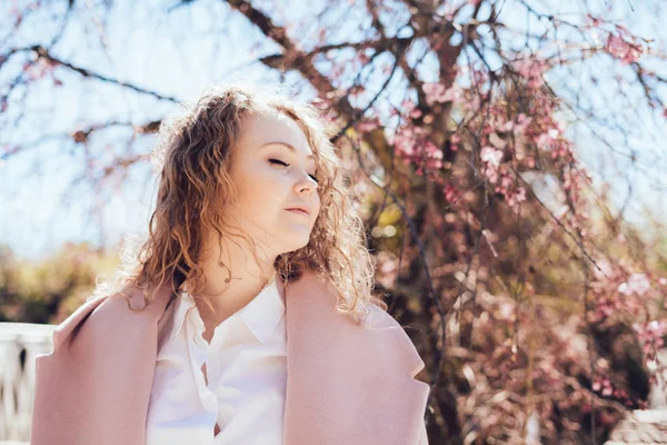 A pacified young woman walks through the park, enjoys spring and warmth, closes her eyes — Stock Photo, Image