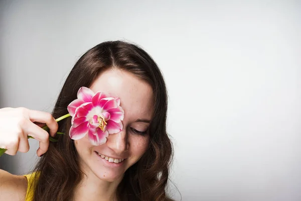 Hermosa mujer encantadora sostiene una flor rosa cerca de la cara y sonríe — Foto de Stock