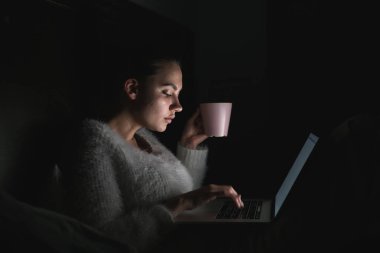 gece geç saatte yatakta oturuyor, onu laptop çalışma ve çay içme iş genç kız serbest meslek