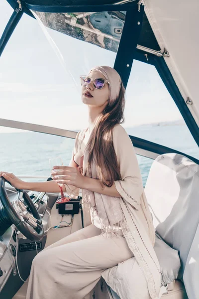 Uma menina elegante de luxo em óculos de sol corre seu iate, velas do mar do Caribe e bebe champanhe — Fotografia de Stock