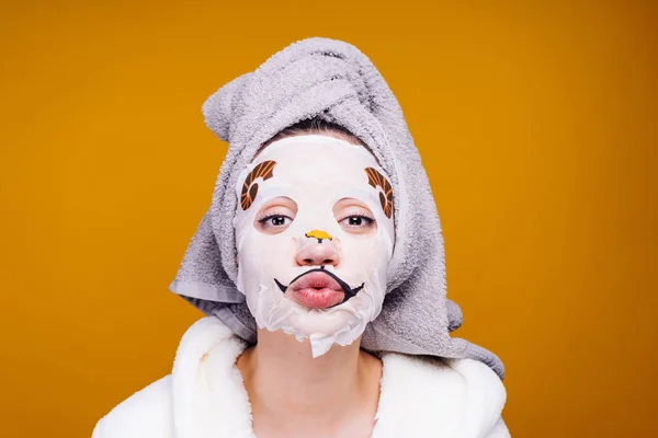 Legrační mladá dívka s ručníkem na hlavě posílá polibek vzduchu, na její tváři hydratační maska s psí tvář — Stock fotografie