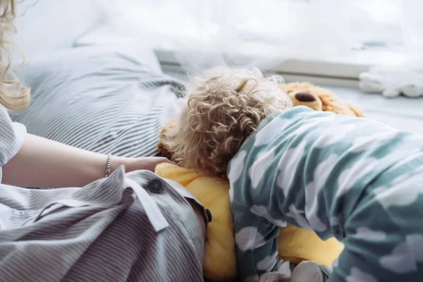 Mamá juega con su pequeño hijo rizado en pijama azul, en la cama, divertirse juntos — Foto de Stock