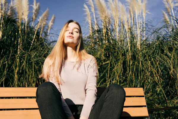 Confiante elegante menina loira posando ao sol, sentado no banco, fechou os olhos — Fotografia de Stock