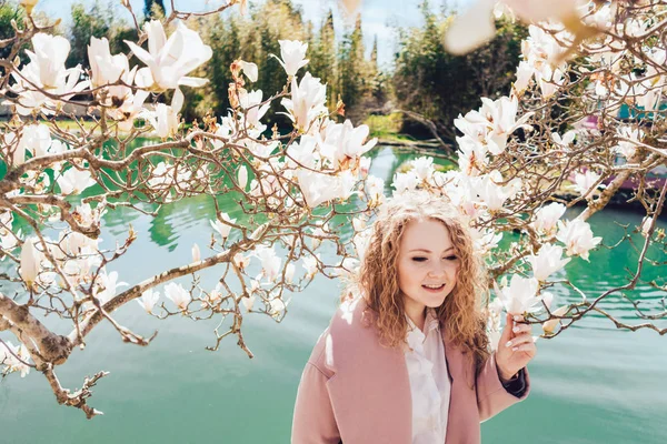 Elegáns göndör fiatal nő élvezi az illata a virágok, a park mellett a tó — Stock Fotó