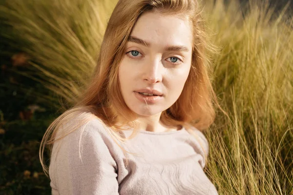 Bela menina de olhos azuis modelo loiro posando na grama ao sol, olhando para a câmera — Fotografia de Stock