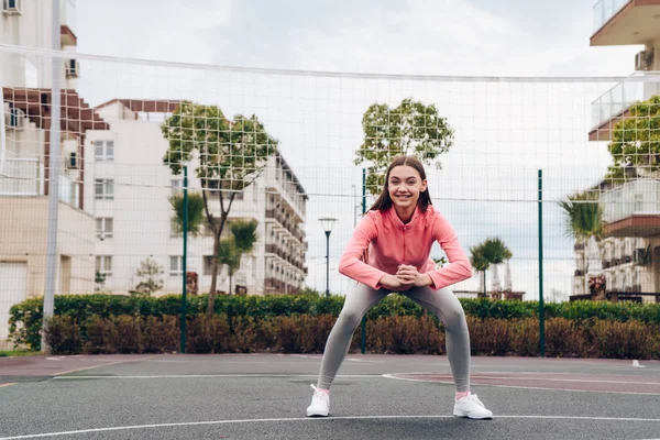 Веселая активная девушка делает упражнения и тренировки на спортивной площадке, приседает — стоковое фото