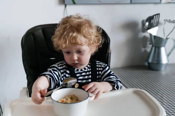 Кудрявый маленький мальчик ест вкусную еду на кухне, семейный завтрак — стоковое фото