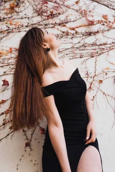 性感长发女孩在一个美丽的黑色礼服摆在花园里的墙上, 休息 — 图库照片