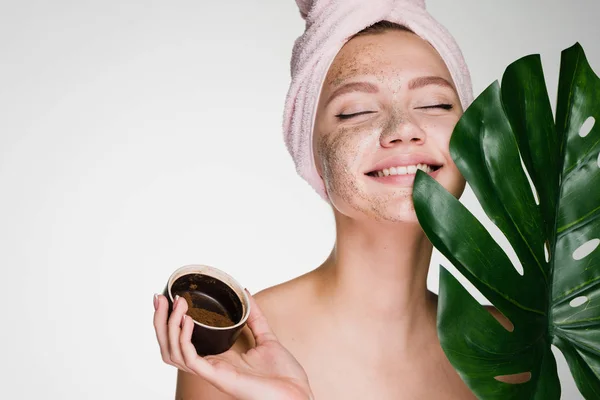 Charmante jong meisje met een handdoek op haar hoofd een nuttige scrub toegepast op haar gezicht, schoonheidsinstituut — Stockfoto