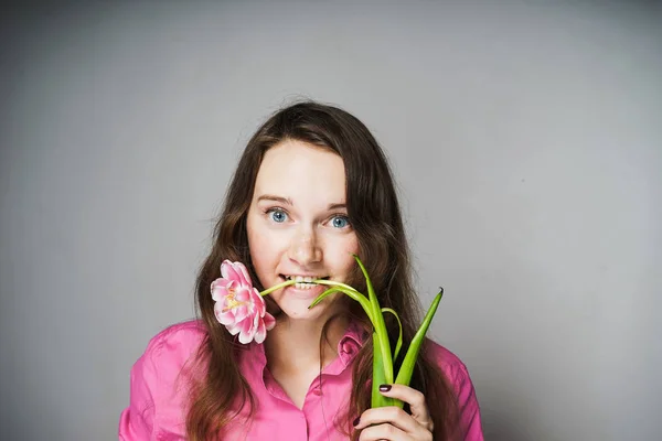 Engraçado jovem trabalhador de escritório mulher em uma camisa rosa mordendo uma flor perfumada e olhando para a câmera — Fotografia de Stock