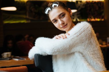 bir restoranda şık bluz oturur bir beyaz kız öğrenci büyüleyici görünüyor kamera ve gülümsüyor