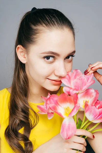 Aantrekkelijke mooi meisje in gele jurk houdt een boeket geurende roze bloemen, glimlachen en kijken naar de camera — Stockfoto