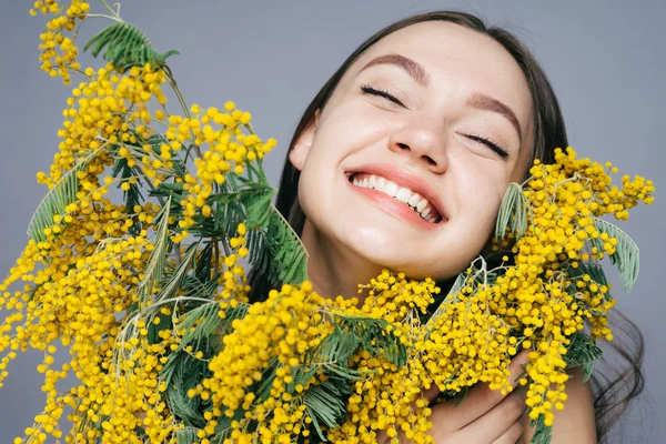幸せな若い女の子を香りのよい黄色いミモザの大きな花束を持って笑みを浮かべて、春を楽しんで — ストック写真
