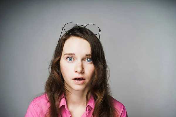 Jovem trabalhador mulher de olhos azuis em uma camisa rosa parece surpreso com a câmera — Fotografia de Stock