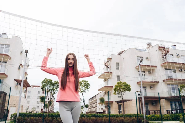 Впевнена спортивна дівчина позує на вулиці біля мережі, граючи у волейбол — стокове фото