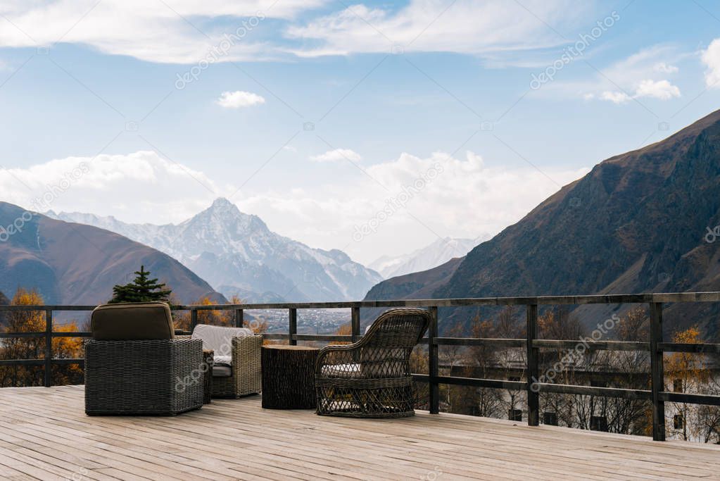 A breathtaking view of the majestic high mountains covered with white snow, a wooden veranda and armchairs
