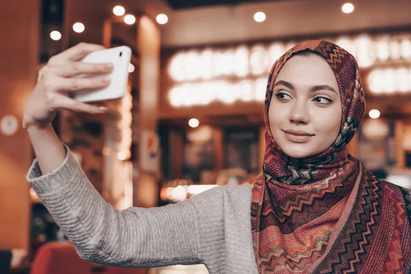 Belle fille musulmane en hijab se trouve dans un bon restaurant, fait du selfie sur son smartphone — Photo