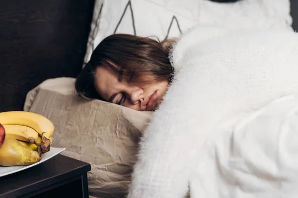 白いパジャマ姿で若い女の子朝の早い段階でのベッドで眠る、アラーム音を聞くことができません。 — ストック写真