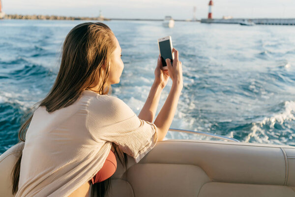 a young stylish girl enjoys a vacation on a yacht, photographing the seascape