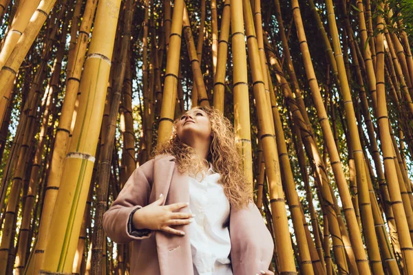 Krullend luxe vrouw poseren tegen een achtergrond van hoge bamboe bomen in een park, houdt van natuur — Stockfoto