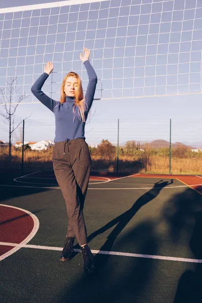 Mooi blond meisje model in stijlvolle kleding poseren op sportveld in de buurt van volleybal net — Stockfoto