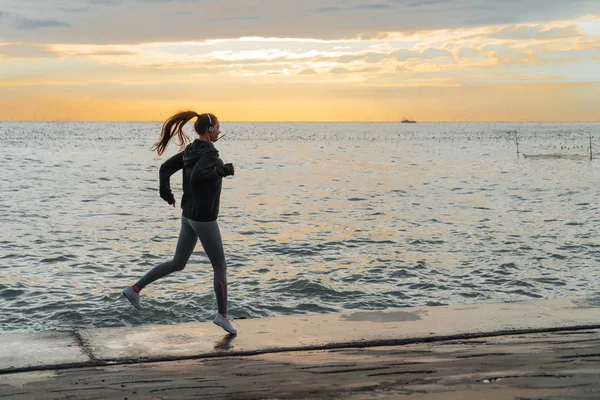 Sport veloce corridore ragazza jogging al mare al tramonto, ascoltando musica sulle cuffie — Foto Stock