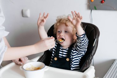çocuk elini yukarı kaldırdı, nazik genç bir anne mutfakta yararlı gıda ile küçük kıvırcık oğlu beslemeleri