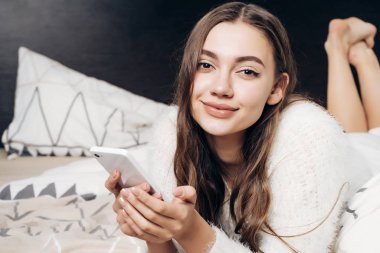bir akıllı telefon tutarak bir günün ardından, dinlenme yatakta yalan güzel uzun saçlı kız
